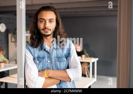 Serious mixed-race businessman with arms crossed by chest standing by open door Stock Photo