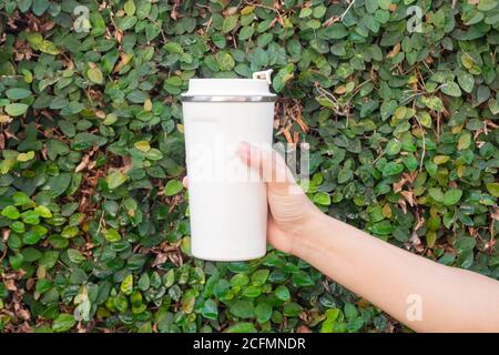 Aluminum thermos mug on hand with green leaves wall, stock photo Stock Photo