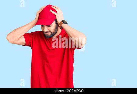 Young handsome man with beard wearing delivery uniform suffering from headache desperate and stressed because pain and migraine. hands on head. Stock Photo