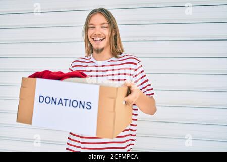 Young caucasian man with blond long hair and beard holding cardboard box with clothes from donations Stock Photo