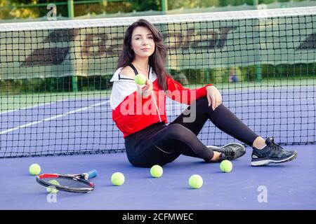 Young pretty woman sitting leaning on tennis net, resting relaxing after training. Portrait of sportswoman on tennis blue court. Healthy life. Stock Photo