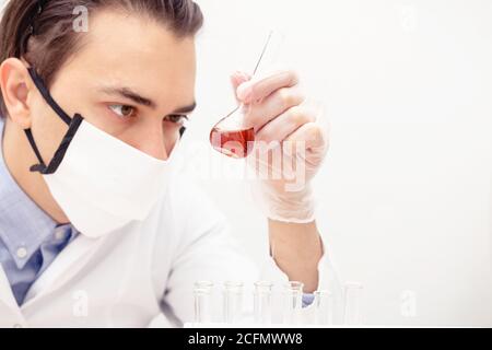 Professional scientist man looking at test-tube with interest. Laboratory assistant mixing liquids for experiment. Flasks on table. Stock Photo
