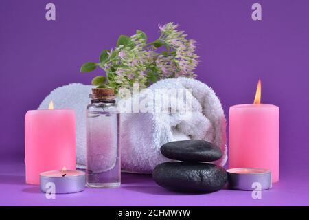 Spa concept background with a pink candle, towel with flowers, and a bottle isolated on purple background Stock Photo