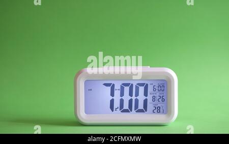 Digital alarm clock on table with green background. Displaying 7:00 am in the morning. Stock Photo