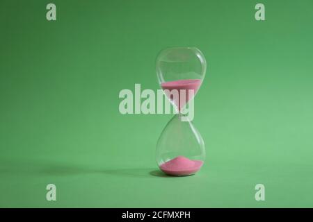 Hourglass with sand flowing on green background. Time passing or classic timer concept. Stock Photo