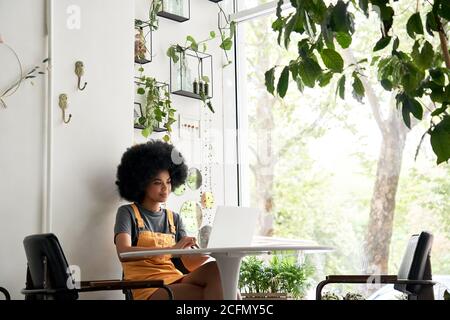 Happy African woman student using laptop sitting at table at home, in cafe. Stock Photo