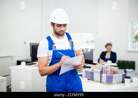 Young construction supervisor in a white helmet taking notes while in office. Stock Photo
