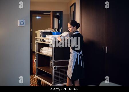 A housekeeping lady in a uniform entering a room with a trolley. Stock Photo