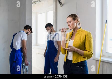 A customer in a jacket speaks on a cell phone. Two builders stand in the background Stock Photo