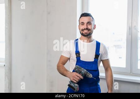 Man in blue overalls posing with a drill and smiling Stock Photo