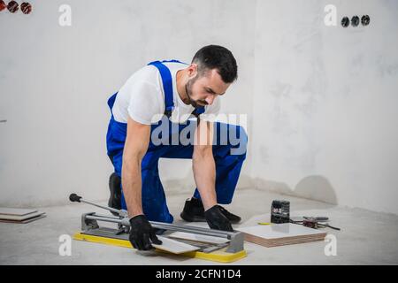 Young man in blue overalls cuts tiles with a special tool Stock Photo