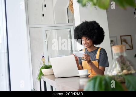 Smiling African woman student watching mobile ad on phone sitting at cafe table. Stock Photo