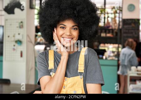 Happy African lady with Afro hair looks at camera stands in cafe, headshot. Stock Photo