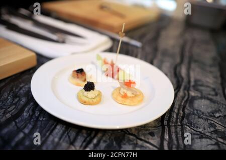 4 small canapes are placed on a white round plate. The table surface is a marble pattern. Selective and blurred focus. Stock Photo