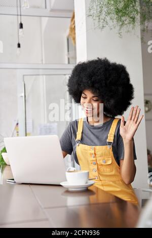 Smiling African woman using laptop video conference calling in cafe. Stock Photo