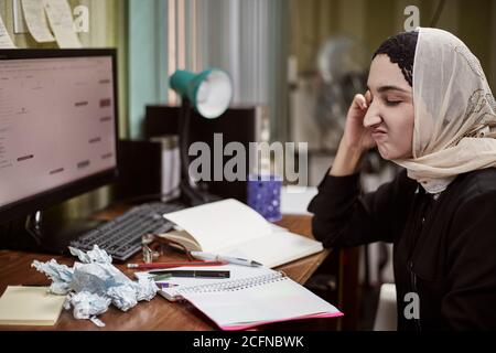 Middle eastern female entrepreneur feeling unhappy. Busy Arabian businesswoman sitting around the heap of papers. Woman in traditional Arabian Stock Photo