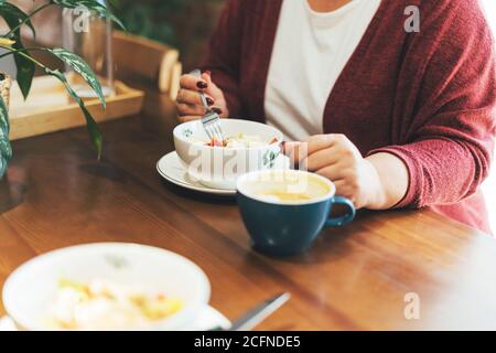 Crop photo of adult brunette woman in glasses in casual clothing plus size body positive having lunch at the cafe Stock Photo