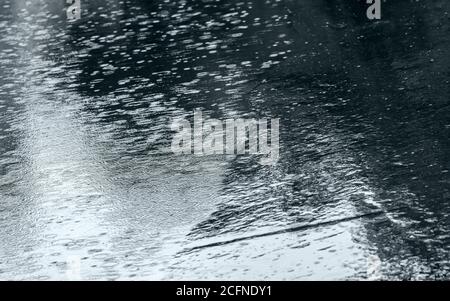 raindrops background with blue sky reflection and water circles on dark asphalt Stock Photo