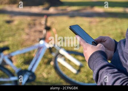 Young man hands texting on his smartphone, in a park, next to his bike, a sunny day Stock Photo