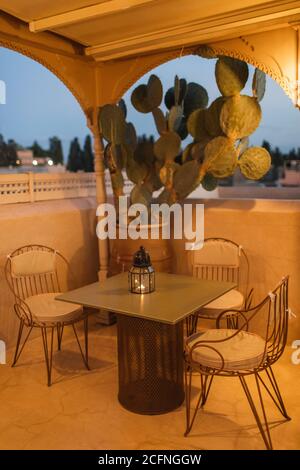 Table for romantic dinner on rooftop terrace in evening. Moroccan style, vintage lamps, candles, cactus flower, twilight. Stock Photo