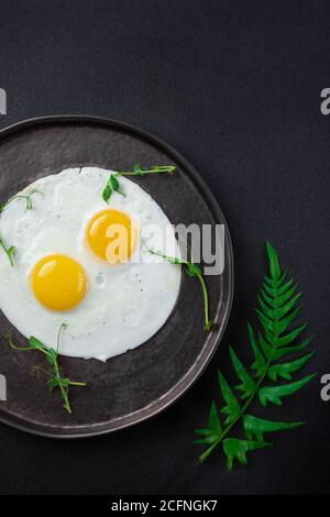 Breakfast with two fried eggs and herbs on black background Stock Photo