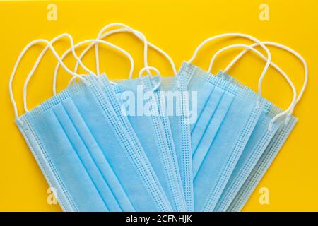 Pile of disposable medical face masks on yellow background. Personal protective equipment, PPE. Stock Photo