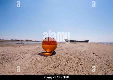 Orange glass ball on sand near the sea. Abstract conceptual photo. Stock Photo