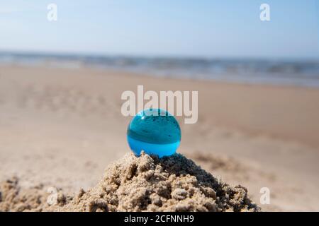 Blue glass ball on sand near the sea. Abstract conceptual photo. Stock Photo