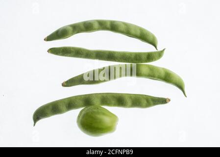 Green under ripe vegetables including a tomato and green beans photographed on a white background. Stock Photo