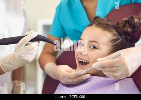 Smiling girl getting tooth curing with luminous dental filling from dentist Stock Photo