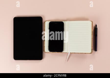 View of a tablet and phone with notebook and pen on pink background Stock Photo