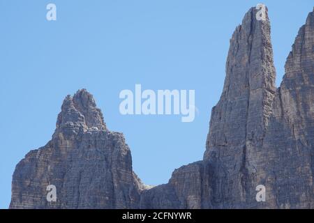 The moon rises in a blue sky above a rocky mountain ridge Stock Photo