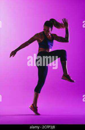 Fit woman doing warm up exercises before a run. Woman athlete working out on purple background. Stock Photo