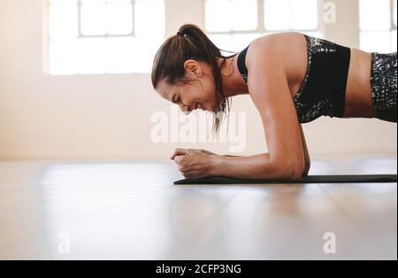 Close up of a strong fitness woman doing plank exercise. Woman doing core workout at a fitness studio. Stock Photo