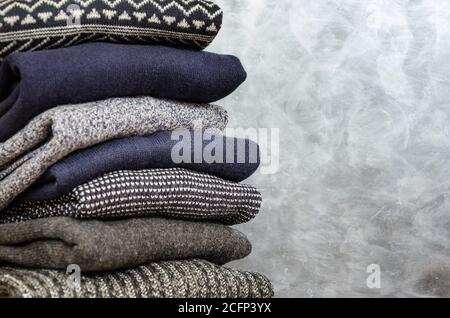 Stack of folded warm knitted men's sweaters on gray background. Copy space. Closeup Stock Photo