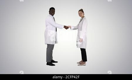 Doctors shaking hands and posing to camera on gradient background. Stock Photo