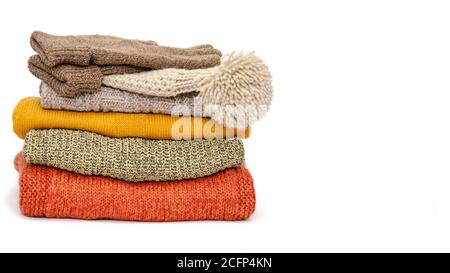A stack of folded knitted warm women sweaters, hat and gloves on a white background. Time to keep warm. Season of warm clothes. Close-up. Copy space Stock Photo