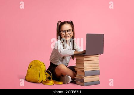 Smiling girl in glasses with backpack sits near stack of books and laptop Stock Photo