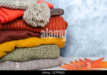 Stack of folded warm knitted women's sweaters, scarf, hat with pompom in warm colors and bright autumn leaves. Close-up. Copy space Stock Photo
