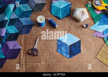 Fragment of tumbling blocks quilt, accessories for quilting on a wooden surface. Stock Photo