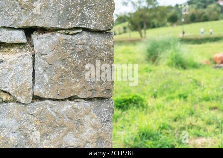 Corner of a stone wall made of rough masonry. Against the backdrop of a wooded hill with green grass and sky. Soft selective focus. Stock Photo