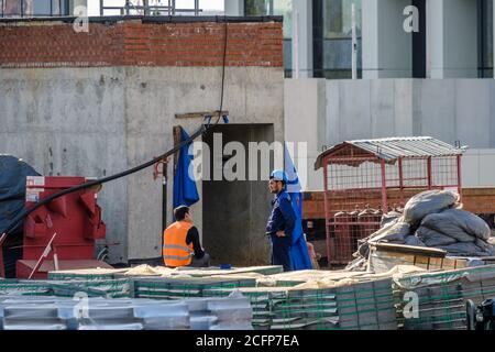 Moscow. Russia. September 06, 2020 Construction workers in uniforms and protective helmets at a construction site among building materials. Summer day Stock Photo