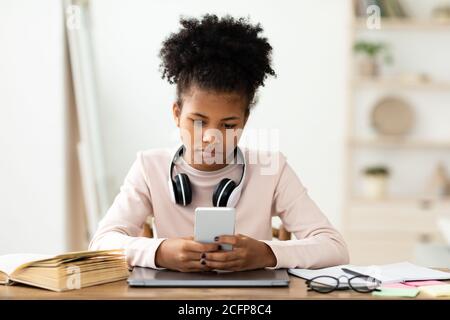 Black Teen Girl Using Phone Sitting At Laptop At Home Stock Photo