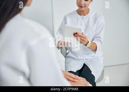 Dermatologist with a gadget sitting by her client Stock Photo