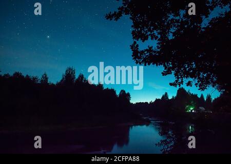 night sky in nature. tourist have a rest in his camp near the forest at night. Man sitting near campfire and tent under beautiful night sky full of st Stock Photo