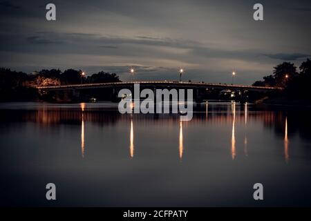 Long exposure photograph of old railway bridge over river at night with reflection in Ratchaburi Thailand Stock Photo