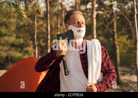 Funny man using axe for shaving in nature Stock Photo