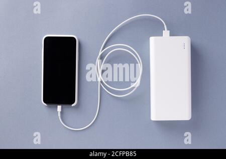 smartphone in a white case is charged from a white Power bank charger. Modern technology. blue background. flat lay Stock Photo