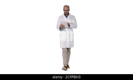 Mature male doctor holding digital tablet using it and walking on white background. Stock Photo