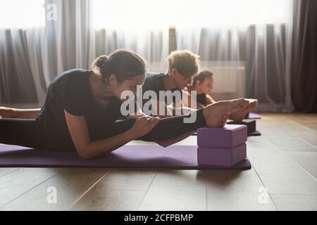 Smiling slim sportswoman stretching legs on mat in gym Stock Photo